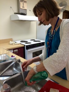 BEFORE: Janet Gaudino, 8th grade science teacher and advisor to JW Cooks, at the small double-basin sinks that date the Teaching Kitchens to a time when very little food was made from whole ingredients. Check back soon for the AFTER picture!