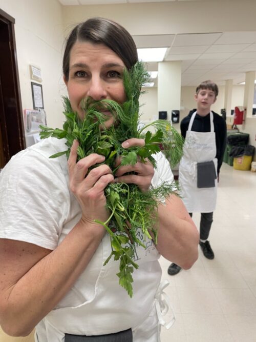 Faculty advisor Betsey Valenza holding herbs as a mustache